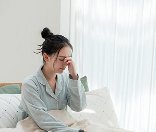 ベッドの上で眠そうに目頭を押さえている女性