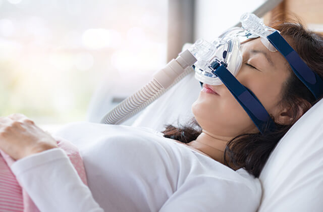 睡眠時無呼吸症候群の治療用マスクをつけて眠っている女性