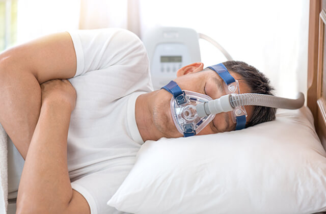 睡眠時無呼吸症候群の治療用マスクをつけて眠っている男性